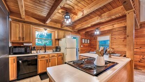Cocina de cabaña de madera con una isla central, armarios de madera, microondas, estufa y refrigerador.
