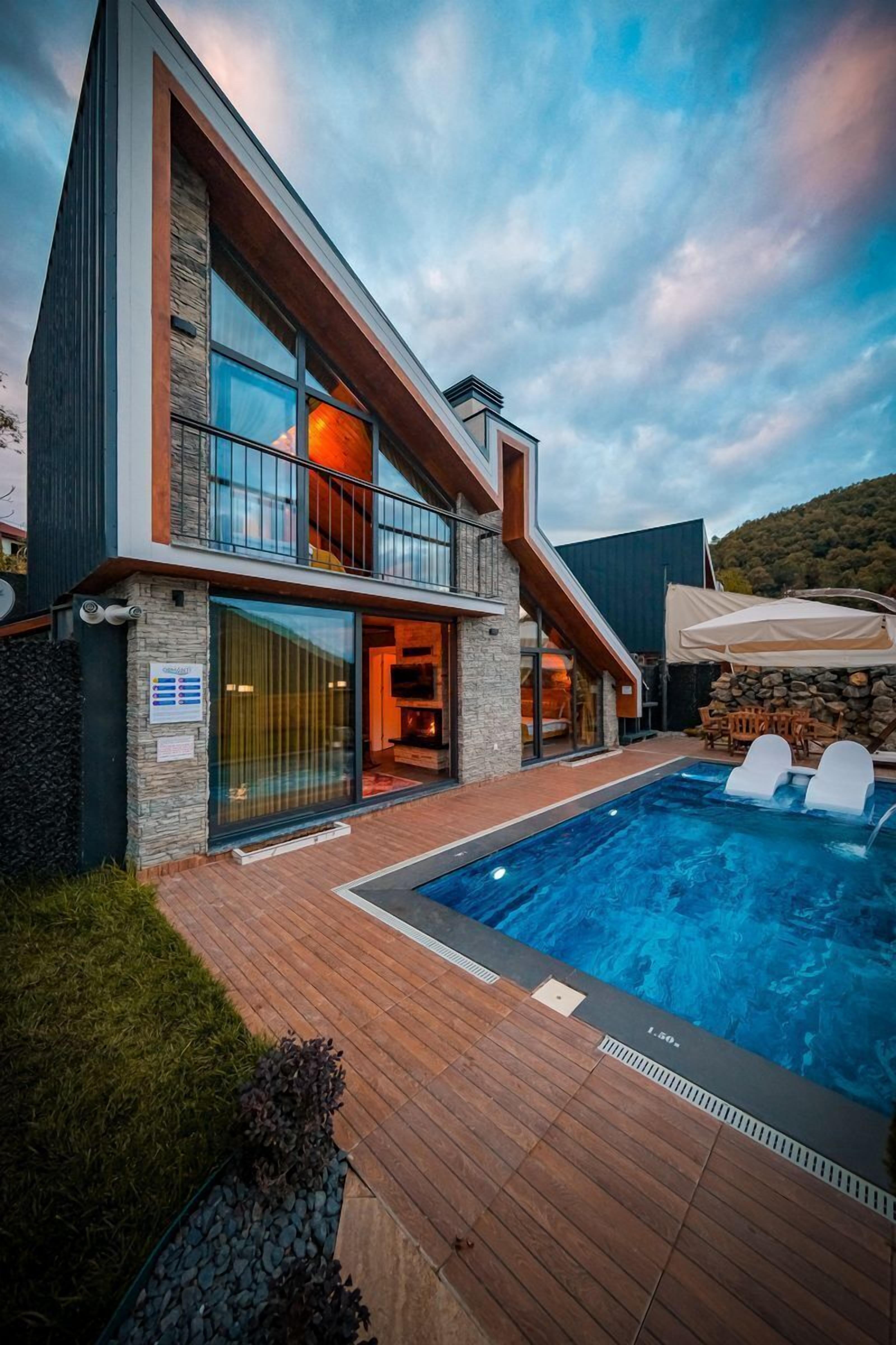 A modern two-story house with a swimming pool, stone walls, and a wooden deck.