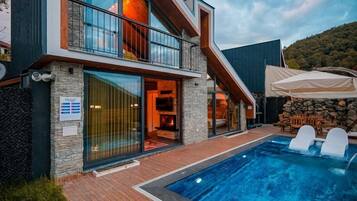 A modern two-story house with a swimming pool, stone walls, and a wooden deck.