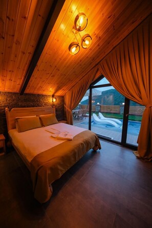 Ein Schlafzimmer mit Holzboden, einem Bett mit weißer Decke und Blick auf einen Swimmingpool.
