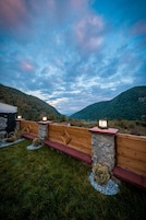 A wooden deck with stone pillars and lanterns, overlooking a mountainous landscape.