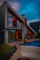 A modern two-story house with a swimming pool, large windows, and a stone facade.