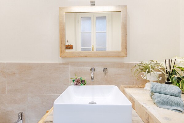 A bathroom with a large bathtub, a wooden-framed mirror, and a tiled wall. - Casa Caretta in Lucca (Lucca)