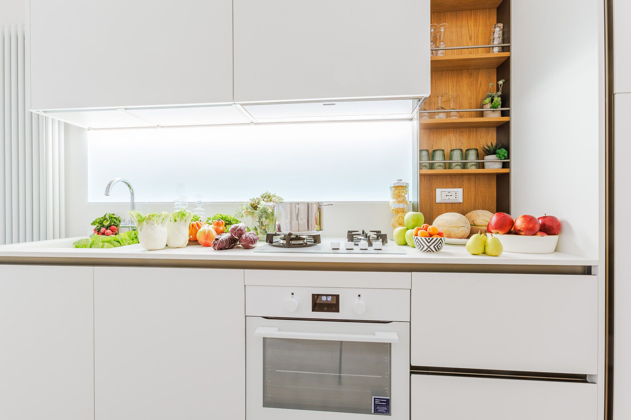 A modern kitchen with a built-in oven, a sink, and a countertop with various fruits and vegetables.