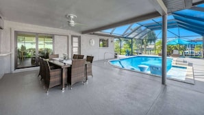 Ein Poolbereich im Innenbereich mit Esstisch und Stühlen, einem Deckenventilator und Blick auf den Außenpool.