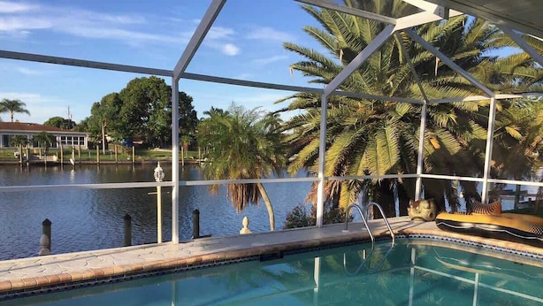 Una piscina interior con agua cristalina, rodeada de palmeras y vistas a una masa de agua.