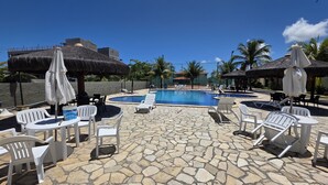 A pool area with stone flooring, white lounge chairs, and thatched umbrellas. - Casa 10 Village I Carneiros by La Playa  (Tamandaré)