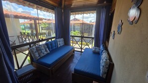 A balcony with a wooden bench and a sofa, both with blue cushions, overlooking a courtyard with buildings and a clear sky. - Casa 10 Village I Carneiros by La Playa  (Tamandaré)