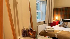 A hotel room with a bed, a bedside table with a red kettle and a white mug, a window with curtains, and a mirror reflecting the room. - Charming 1-bedroom cottage - the perfect couples escape! (Mossdale, Castle Douglas)