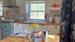A kitchen with a wooden table, a sink, and a window. There are flowers on the table and a chair in front of it. - Charming 1-bedroom cottage - the perfect couples escape! (Mossdale, Castle Douglas)