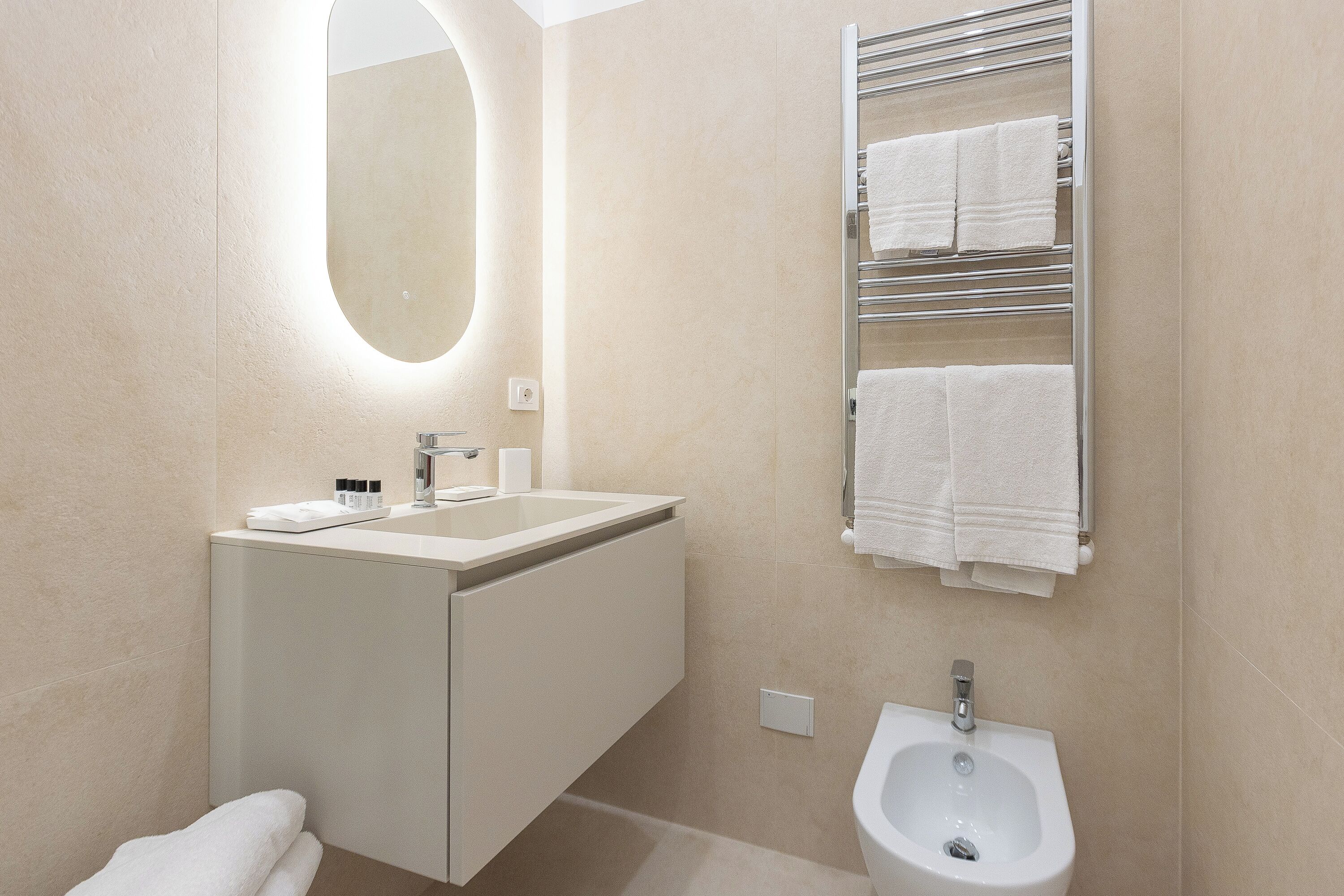 A modern bathroom with a sink, mirror, towel rack, and bidet.