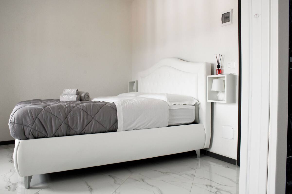 Une chambre d’hôtel moderne avec un lit bien fait, une table de chevet avec une lampe et une étagère murale contenant des articles de toilette.