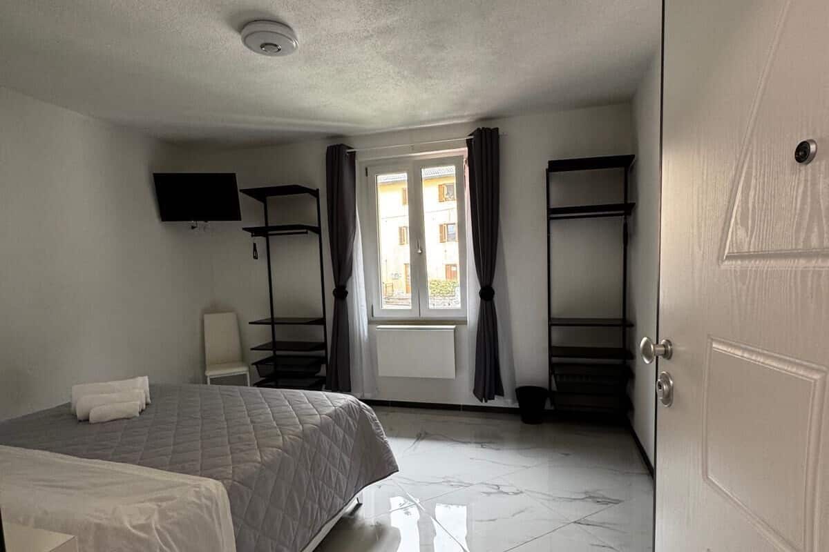 Une chambre d’hôtel avec un lit, un bureau, une chaise, une télévision et une fenêtre avec des rideaux.