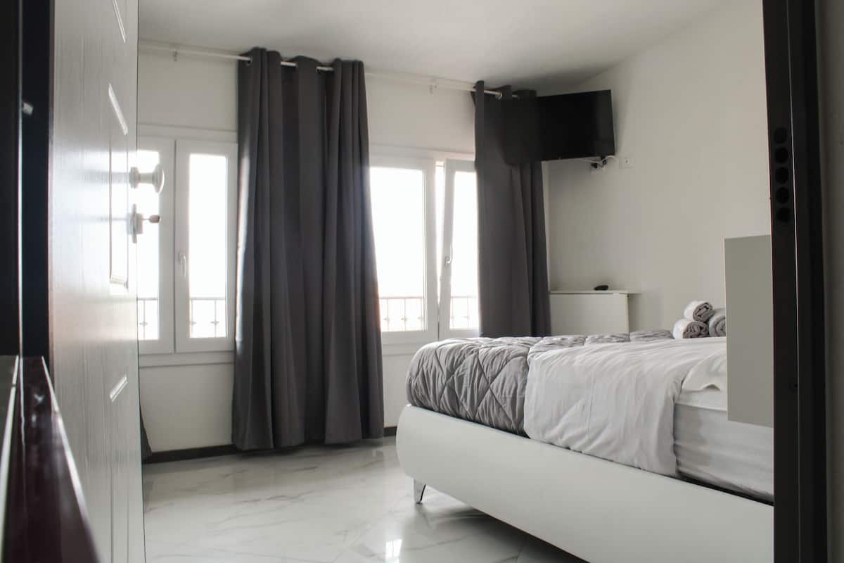 Une chambre à coucher avec un lit, un téléviseur fixé au mur et une fenêtre avec des rideaux.