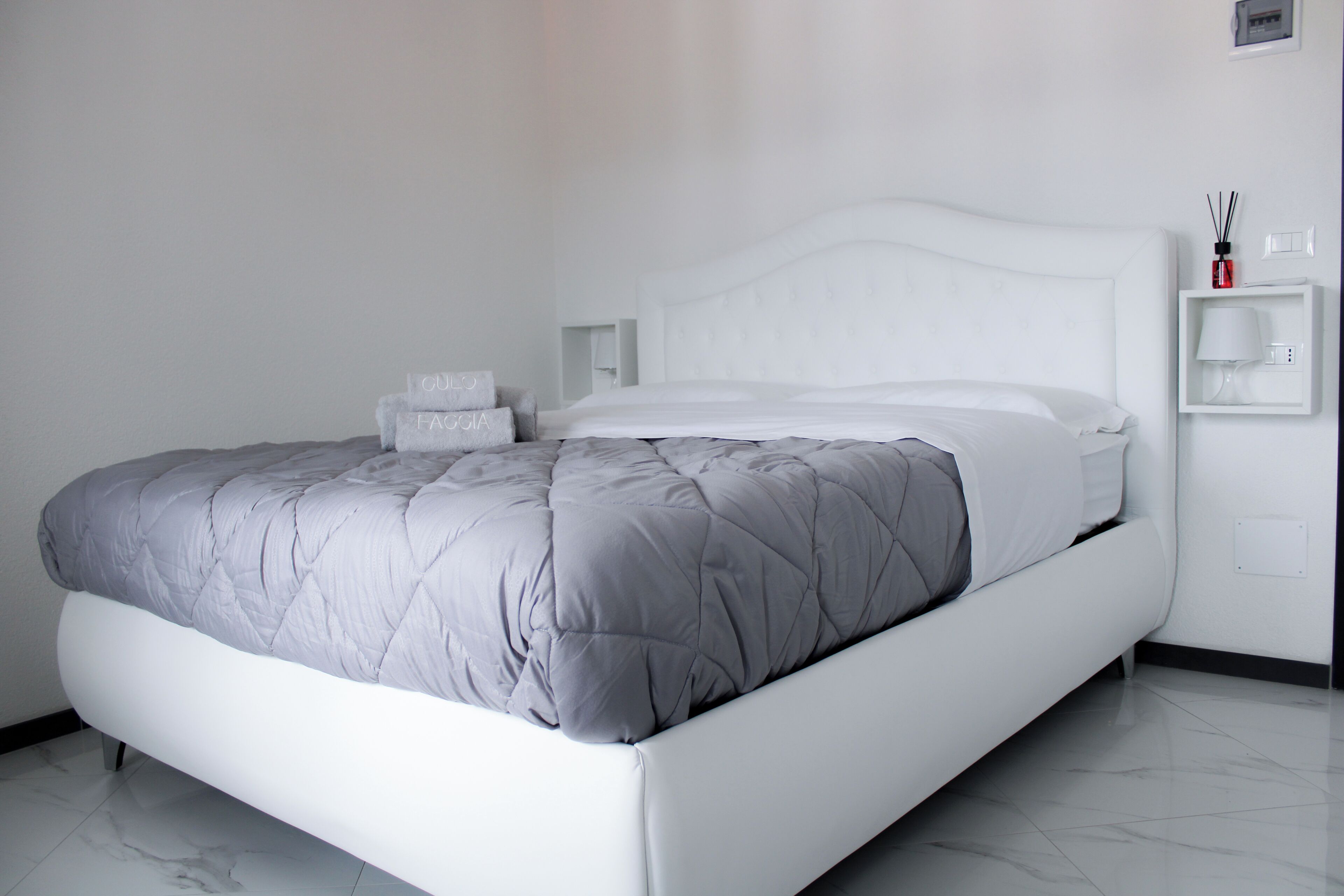 Ein modernes Schlafzimmer mit einem weißen Bett, grauer Bettwäsche und einem Marmorboden.