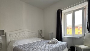 A neatly arranged bedroom with a large bed, a chair, a window with curtains, and a radiator. - La rosa dei Pepoli (Castiglione dei Pepoli)