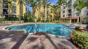 A swimming pool surrounded by palm trees and a multi-story building with balconies.