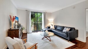 A modern living room with a leather sofa, glass coffee table, and a view through a large window.