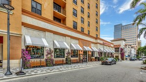 A hotel with outdoor seating, a checkered pavement, and a street view.