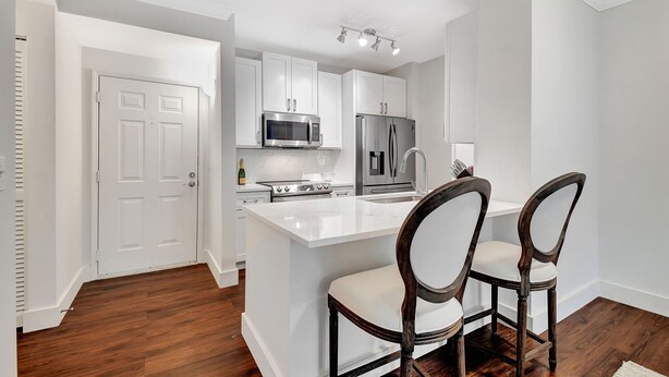 A modern kitchen with white cabinetry, stainless steel appliances, and a central island with two chairs.