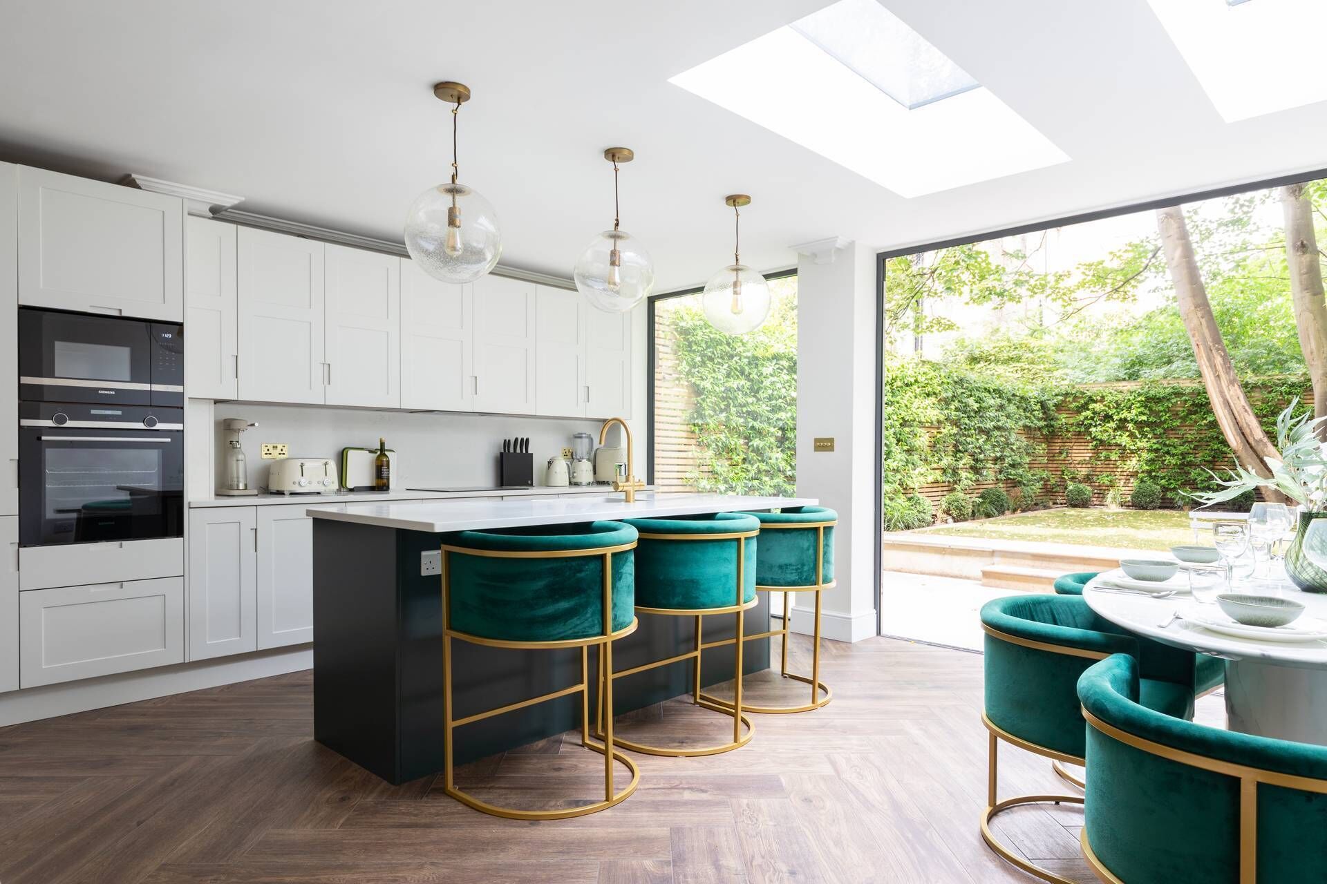 A modern kitchen with white cabinets, a central island with teal bar stools, and a skylight.