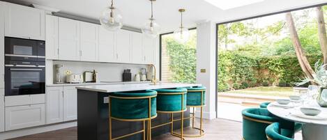 A modern kitchen with white cabinets, a central island with teal bar stools, and a skylight.