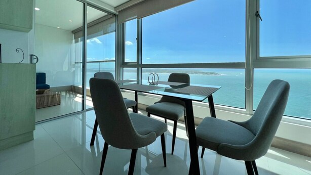 A modern room with a glass table and chairs, large windows offering a view of the sea.
