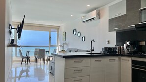 A modern kitchen with a central island, white cabinetry, and a view of the sea through large windows.