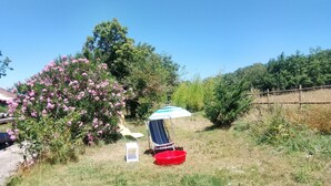 A grassy area with a small white table, a red basin, and a striped umbrella.
