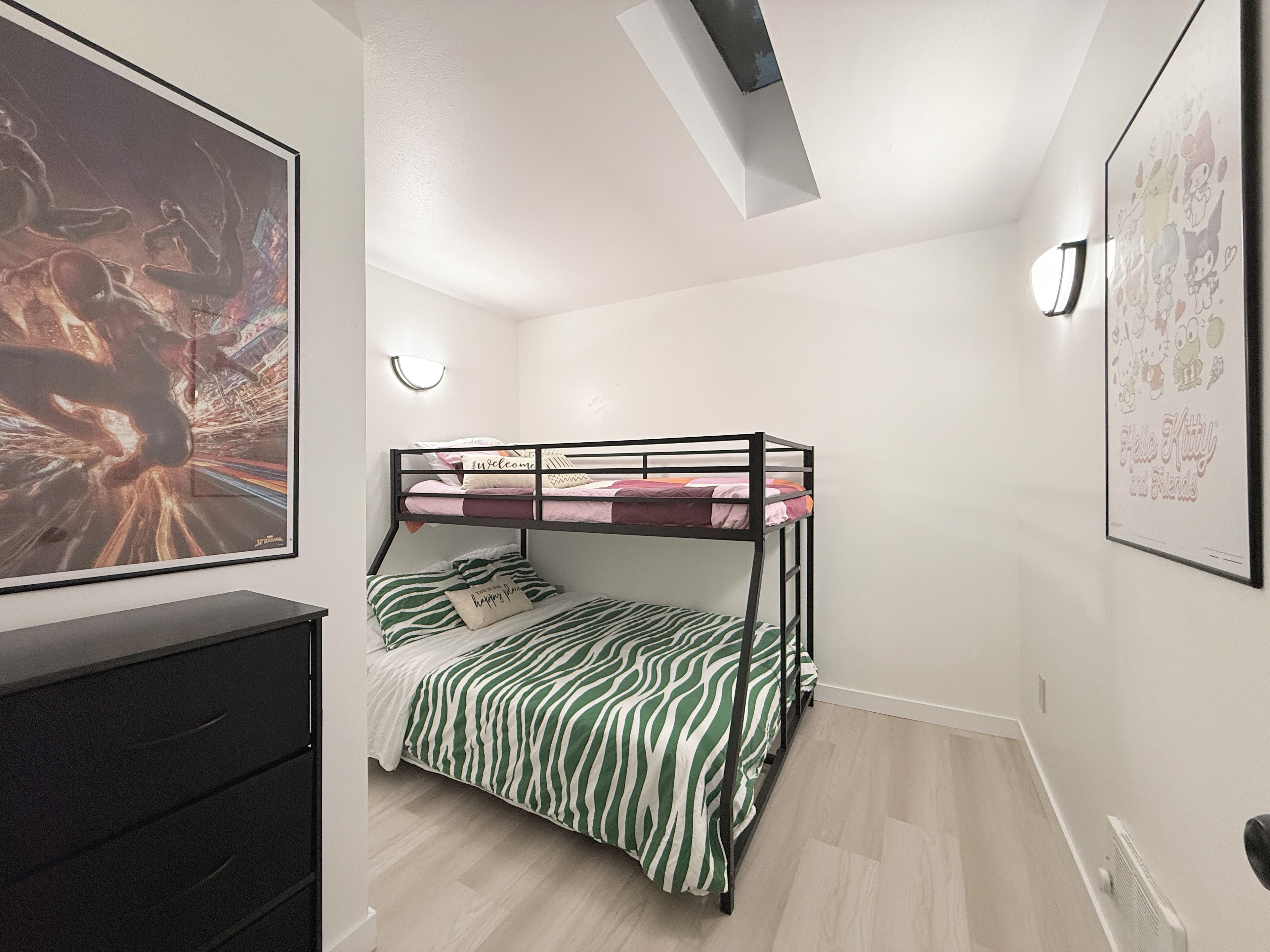 A bunk bed with a zebra print bedspread, a black dresser, a framed poster on the wall, and a ceiling light.