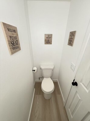 A small, clean bathroom with a white toilet, wooden floor, and three wooden signs on the walls. - Lovely 3-bedroom townhome in Seattle near U of Washington (Seattle)