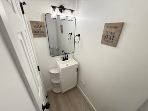 A small bathroom with a white sink, mirror, and light fixture. There are two signs on the wall, one saying "The SOAP IS NOT JUST FOR DECORATION" and the other "WELCOME PLEASE SEAT YOURSELF". - Lovely 3-bedroom townhome in Seattle near U of Washington (Seattle)