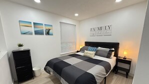 Un dormitorio con cama, mesita de noche, cómoda, ventana con persianas y decoración en la pared.
