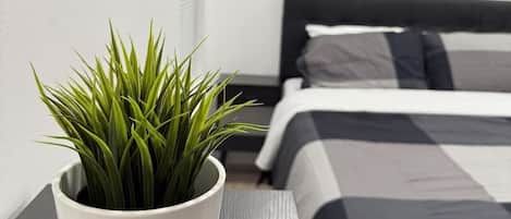 A neatly arranged bedroom with a bed, a bedside table with a potted plant, and a wall with framed text.