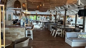 Ein offenes Restaurant mit Korbmöbeln, einer Bar und Blick ins Freie.