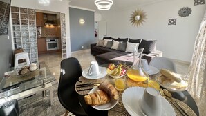 A modern living room with a dining area, featuring a sofa, a coffee table, and a kitchen in the background.