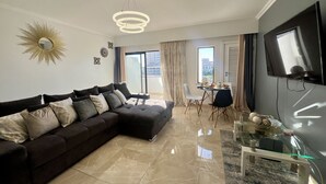 A modern living room with a sectional sofa, a dining area, and a TV mounted on the wall.