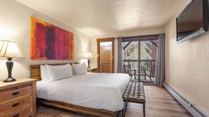 Ein Schlafzimmer mit einem hölzernen Bett, zwei Nachttischlampen, einer Bank, einem großen abstrakten Gemälde und einem an der Wand montierten Fernseher.