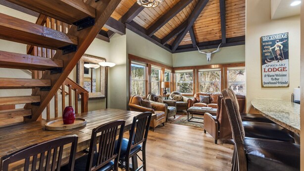 Eine Holztreppe, ein Essbereich mit Holztisch und -stühlen, ein Wohnzimmer mit Sofas und Kamin, und ein Schild, das das Breckenridge Lodge bewirbt.