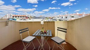 Un balcón con dos sillas y una mesa, vista de edificios y cielo despejado.