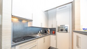 Una cocina moderna con armarios blancos, encimera negra y electrodomésticos de acero inoxidable, incluyendo una placa de inducción y una cafetera.