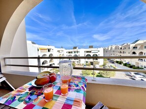 Een balkon met een tafel voor twee, met een kleurrijke tafelkleed, een karaf en twee glazen jus d'orange.