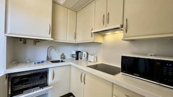 A compact kitchen with white cabinets, a built-in microwave, a coffee maker, and a dishwasher.