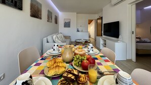 Un comedor con una mesa preparada para el desayuno, un sofá, un televisor y una puerta que da a otra habitación.