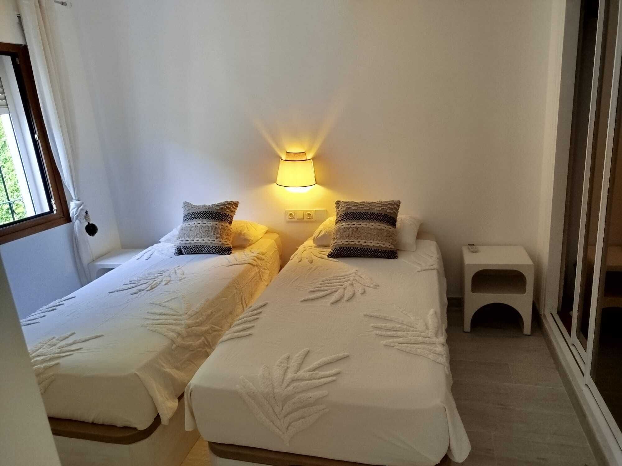 Una stanza accogliente e piccola con due letti, un comodino e una lampada.