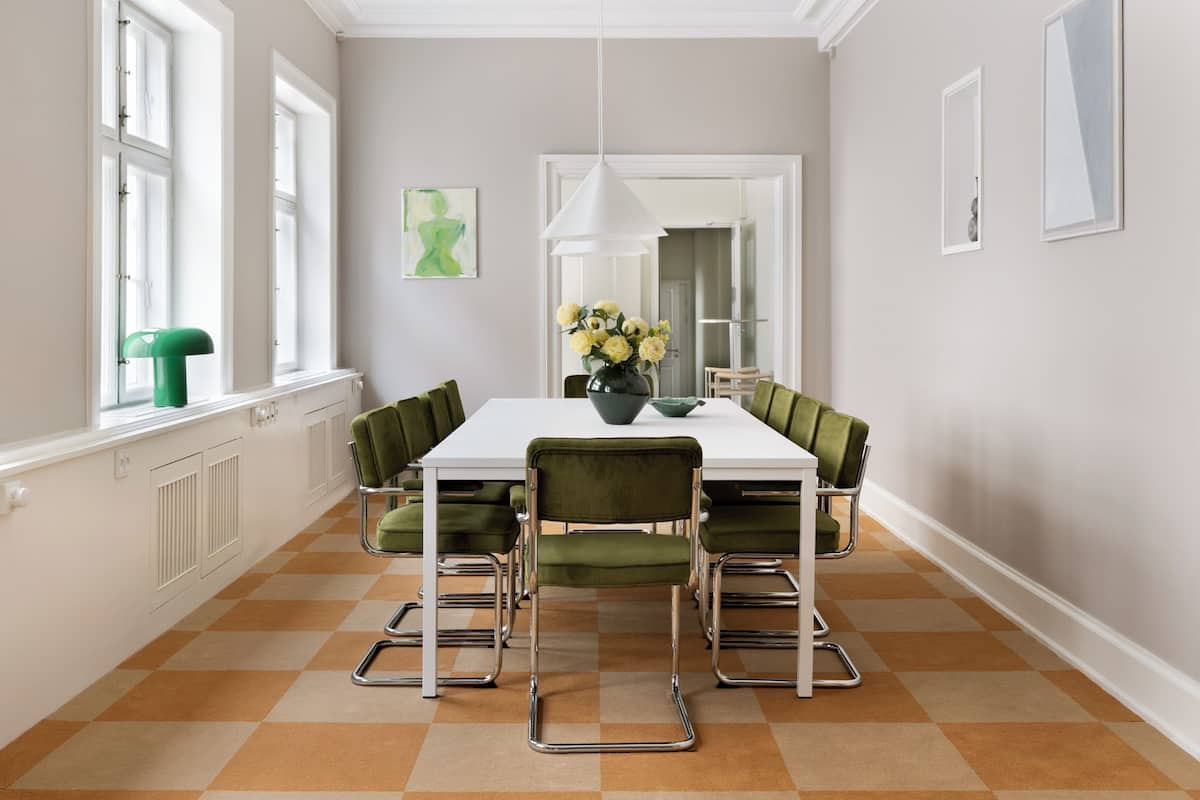 Een eetruimte met een witte tafel, groene stoelen en een bloevas.