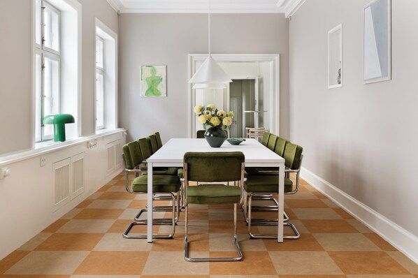 Een eetruimte met een witte tafel, groene stoelen en een bloevas.