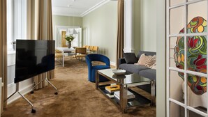 A spacious living room with a flat-screen TV, a coffee table, a sofa, and a dining area in the background.