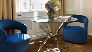 A room with a glass table, two blue chairs, a vase with flowers, and a window with curtains.