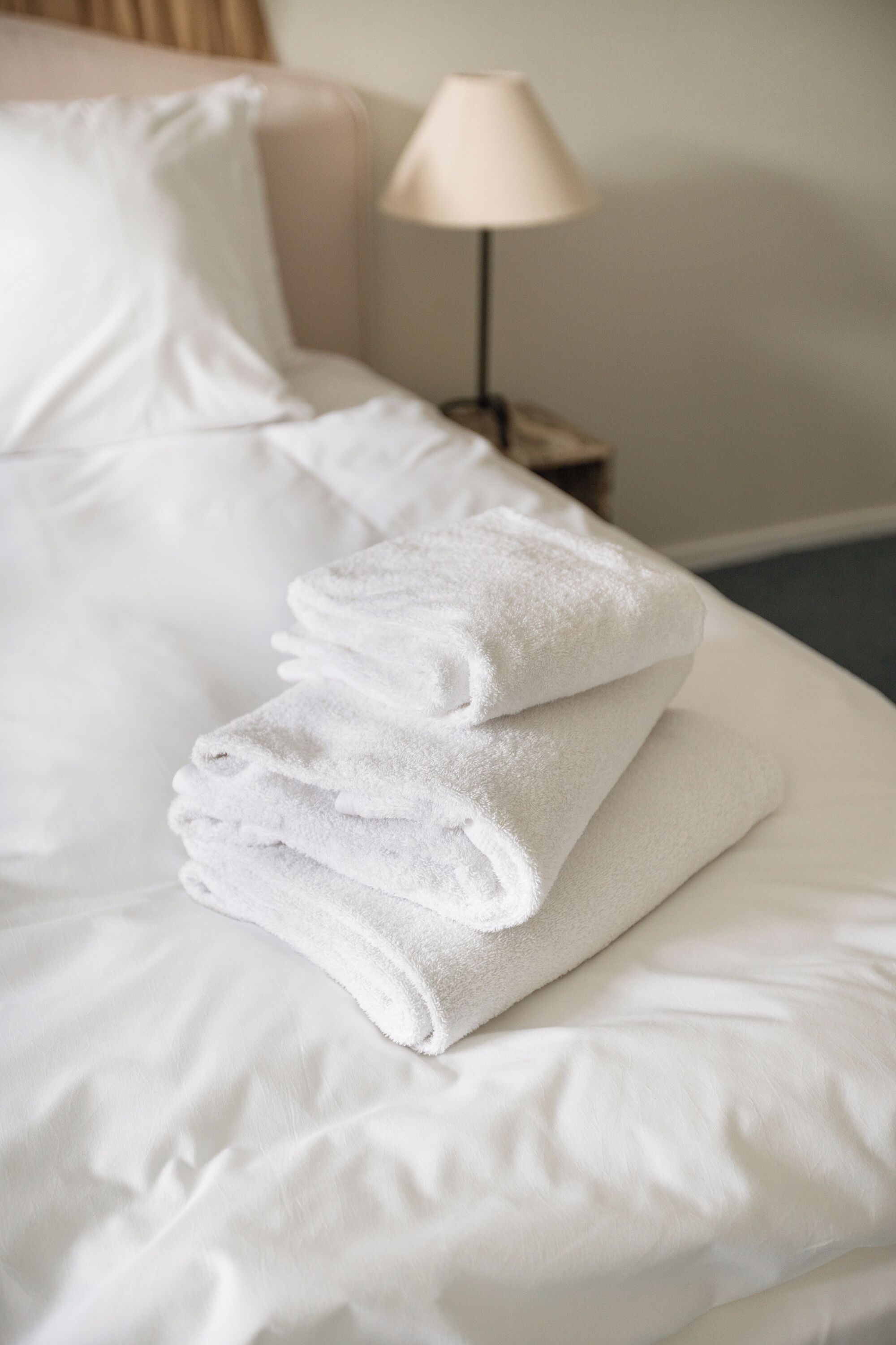 A neatly made bed with white linens and a stack of folded white towels.